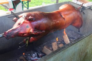 Pork being roasted with a stick crossing its body.