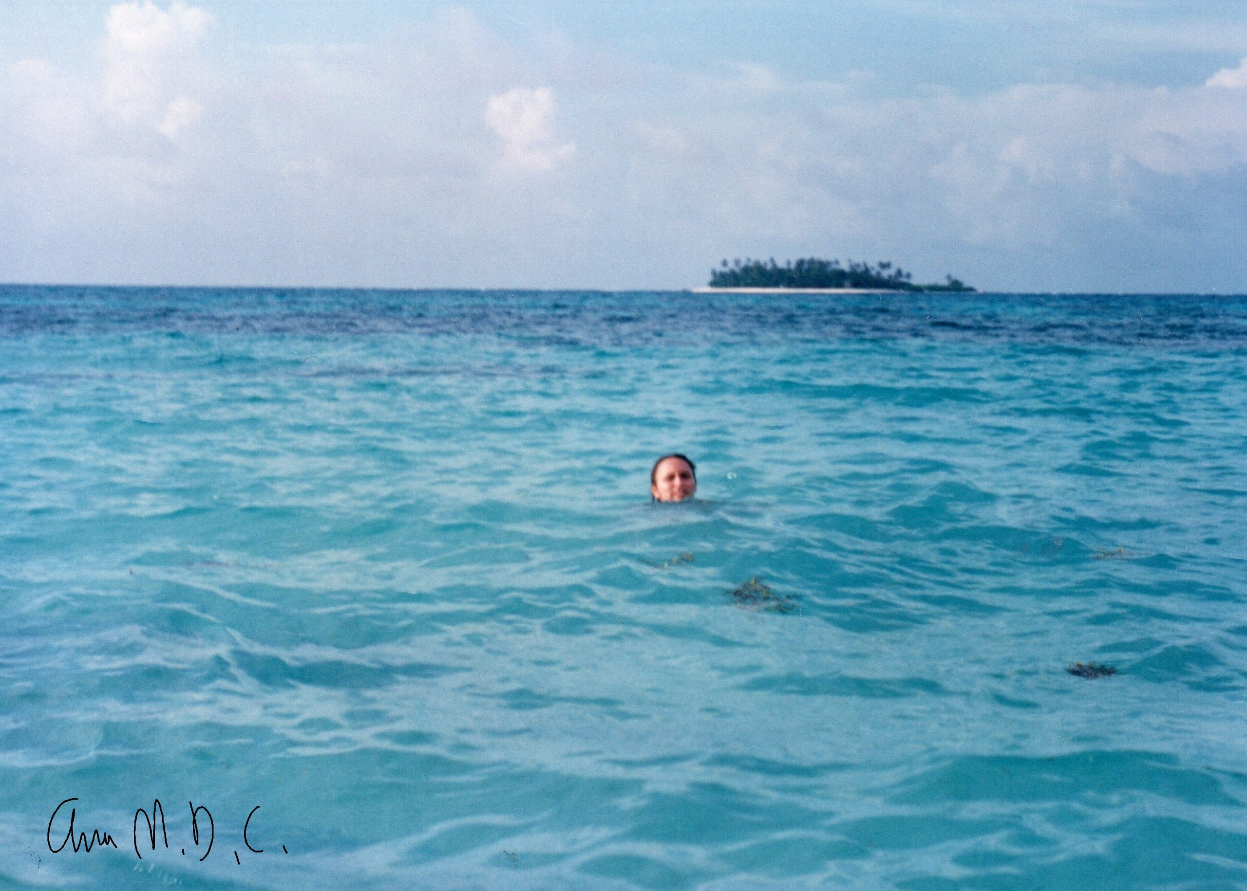 Small island in the back of light blue sea with the head of someone